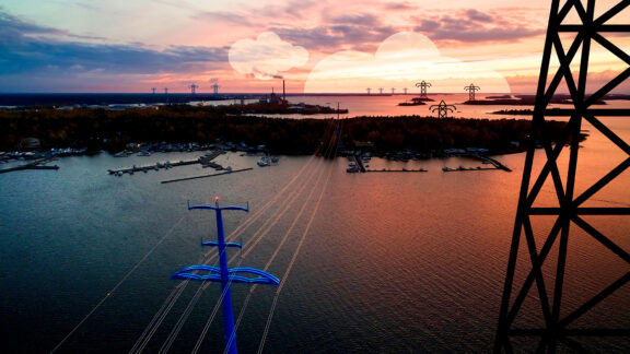 Vaskiluoto kuvattuna ilmasta Palosaaren suunnalta. Keskellä kulkee Vaskiluodon ja Palosaaren välinen voimajohtolinja, etualalla suuri voimajohtopylväs merialueella. Oikeassa reunassa myös kuvitus voimajohtopylväästä, lisää pylväskuvituksia kauempana horisontissa.