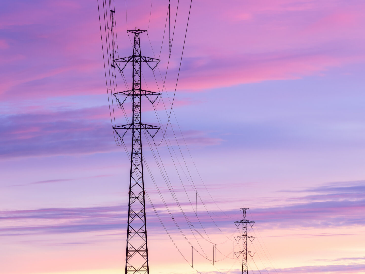 Kaksi voimajohtopylvästä upeaa taivasta vasten auringon laskiessa.