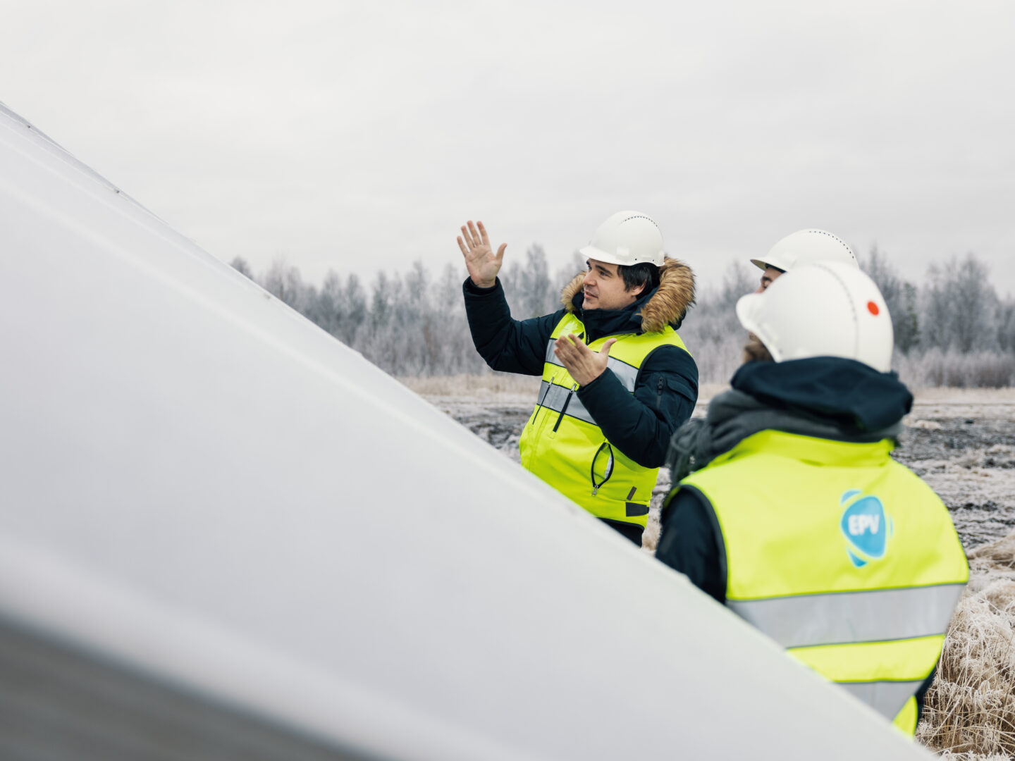 Kolme henkilöä juttelemassa suuren aurinkopaneelin edessä huomioliivit päällään ja suojakypärät päässään.